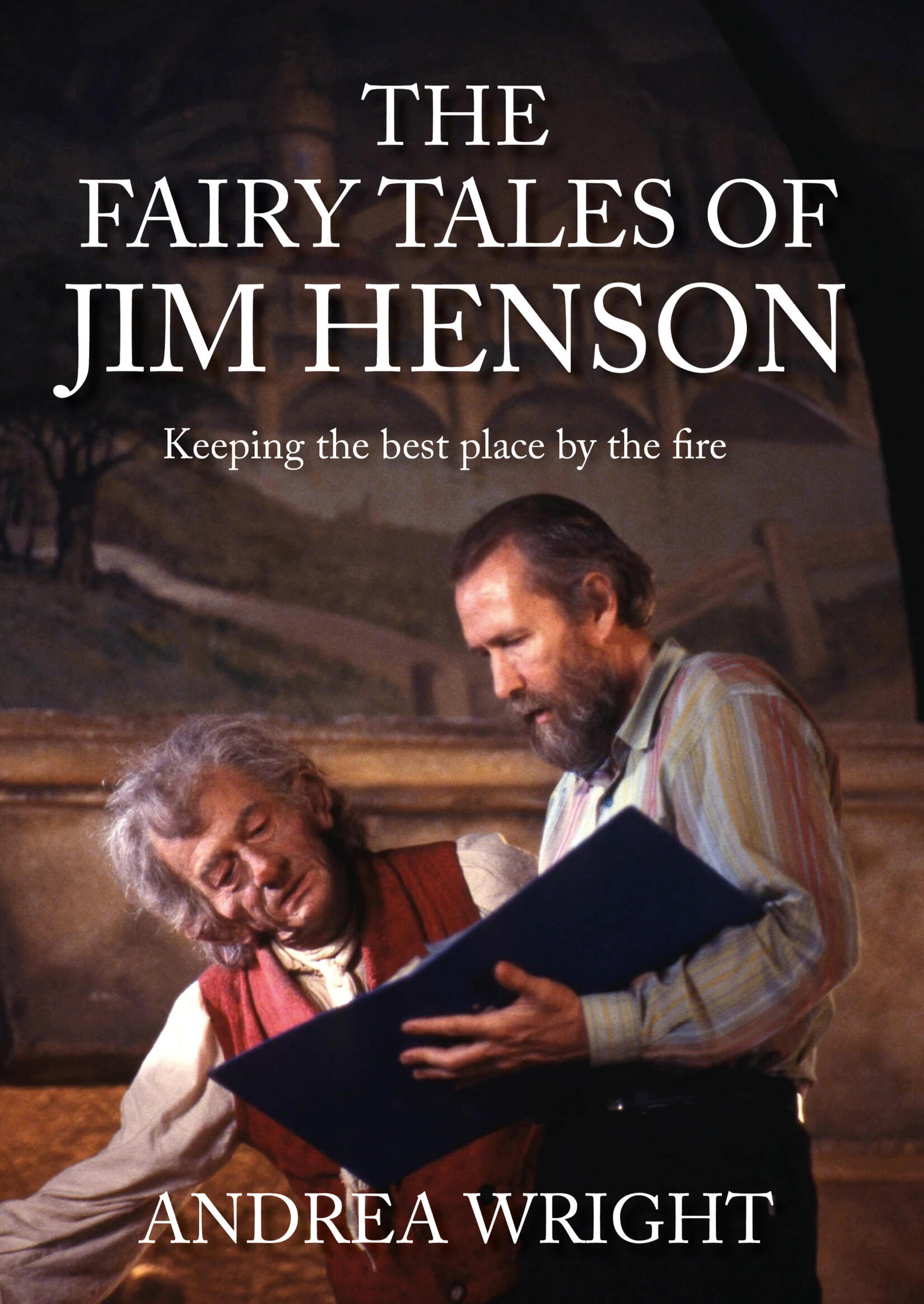 Book cover: The Fairy Tales of Jim Henson — Keeping the best place by the fire, by Andrea Wright. Jim Henson leans over an open folder beside a puppet of a white-haired storyteller in a red waistcoat, both lit against a painted backdrop.
